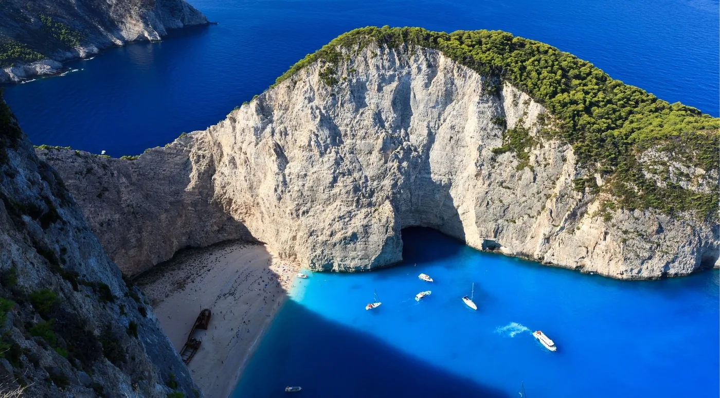 Aerial view of Navagio bay showing the natural rock arch, white cliffs and boats anchored offshore in deep blue water