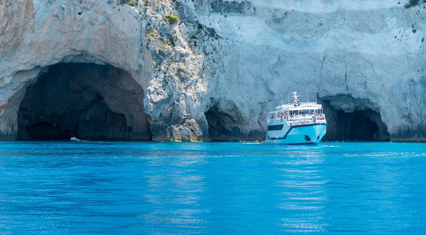 A white tour boat floating at the entrance to the Blue Caves beneath weathered white cliffs