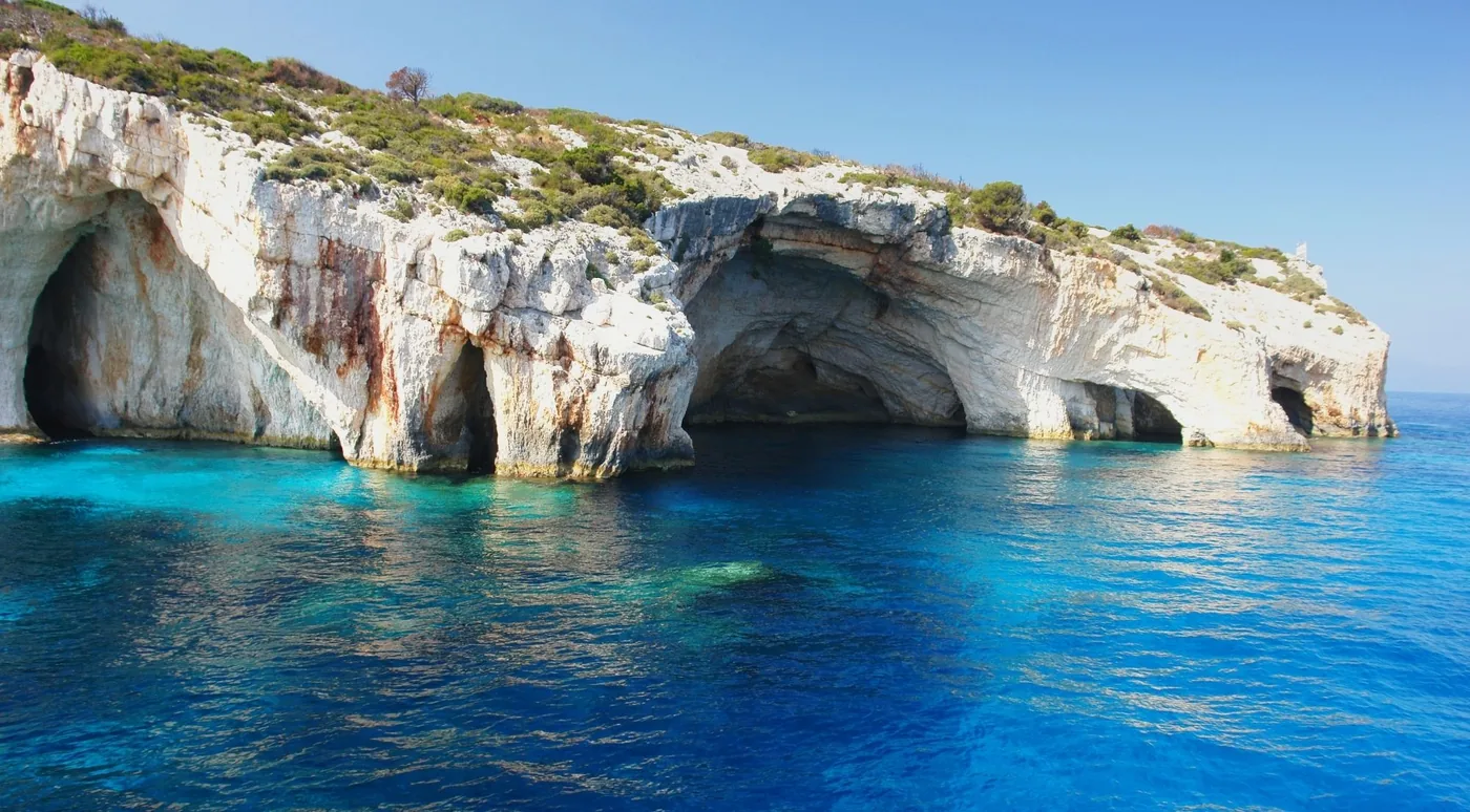 Multiple arched cave openings in white limestone cliffs above clear turquoise water