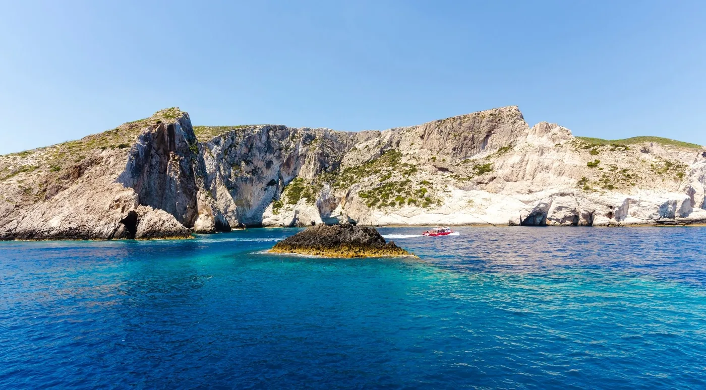 A rocky headland with natural arches and a small boat on calm blue water under a clear sky