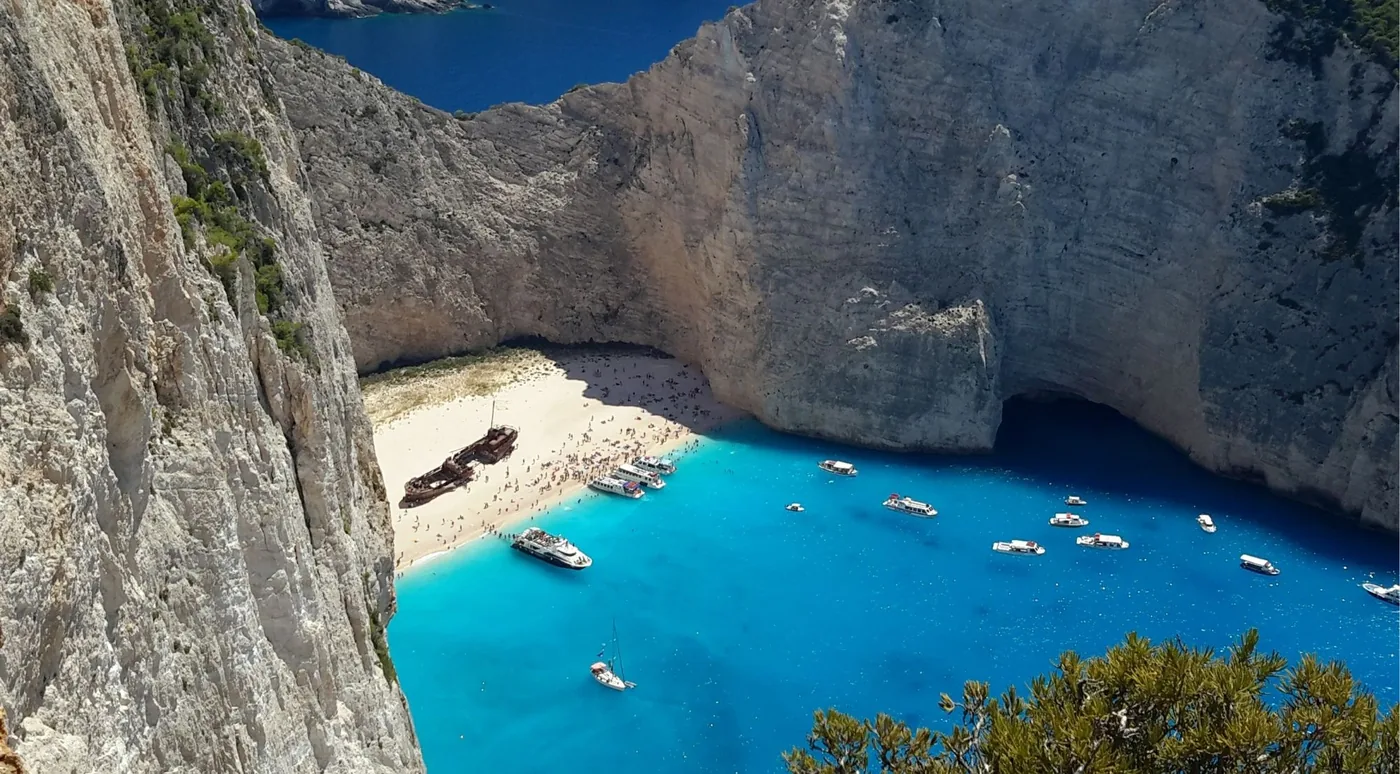 Navagio bay viewed from the clifftop with several tour boats gathered on the turquoise water near the shore