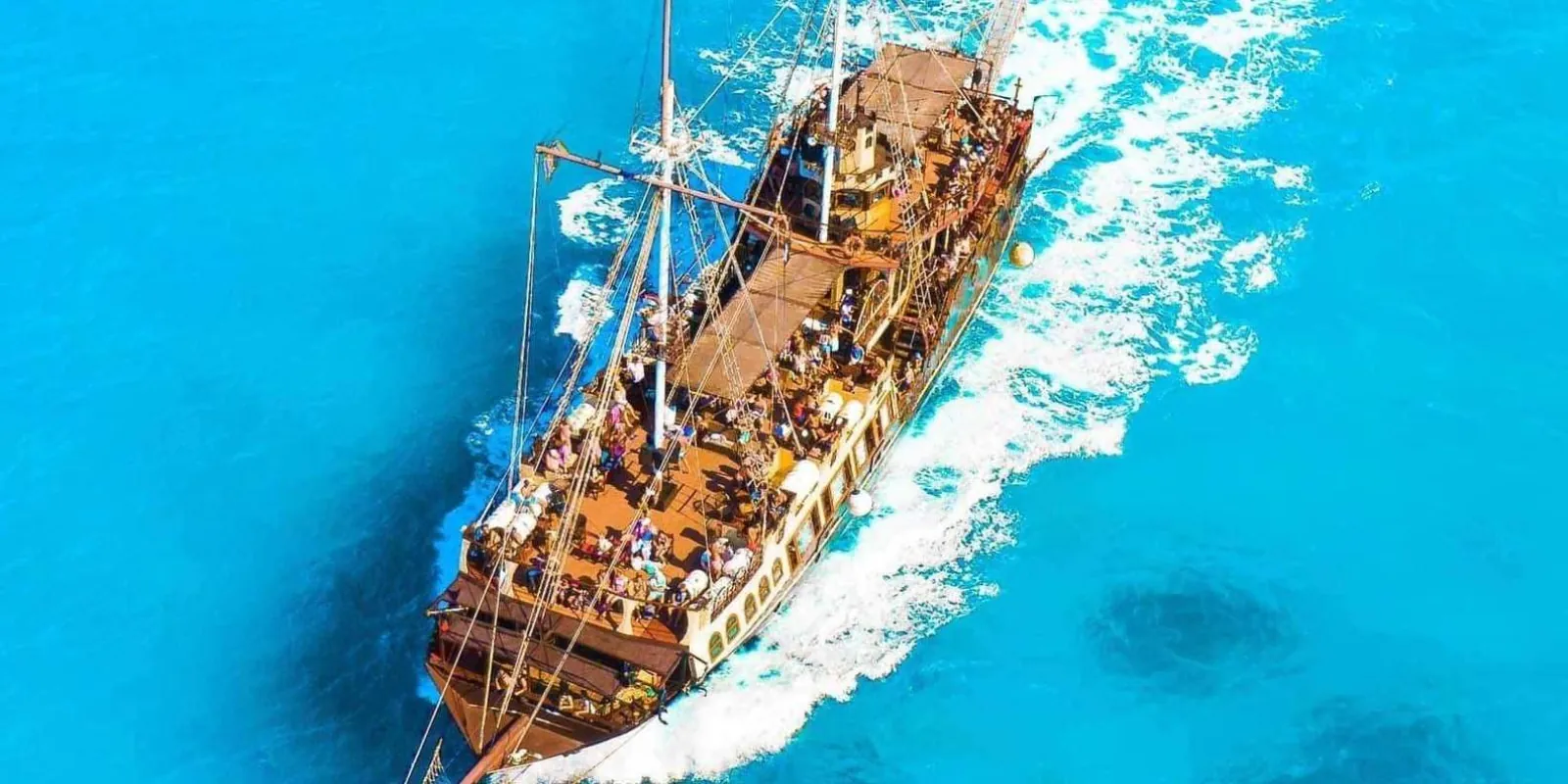 The pirate ship under way on brilliant blue water, seen from above