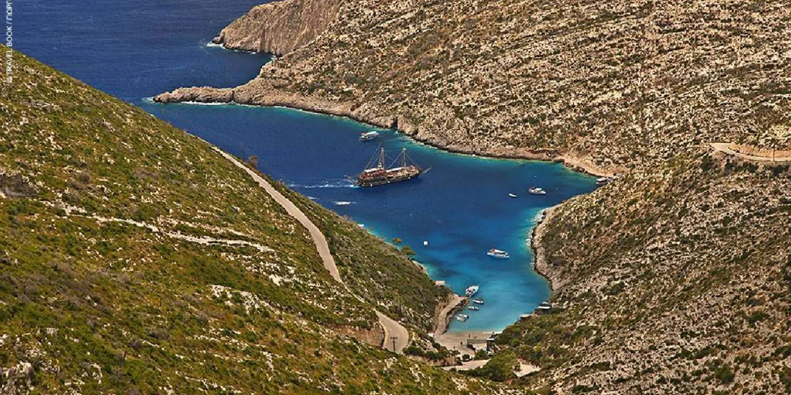 An aerial view of a steep green headland with the pirate ship anchored in the bay below