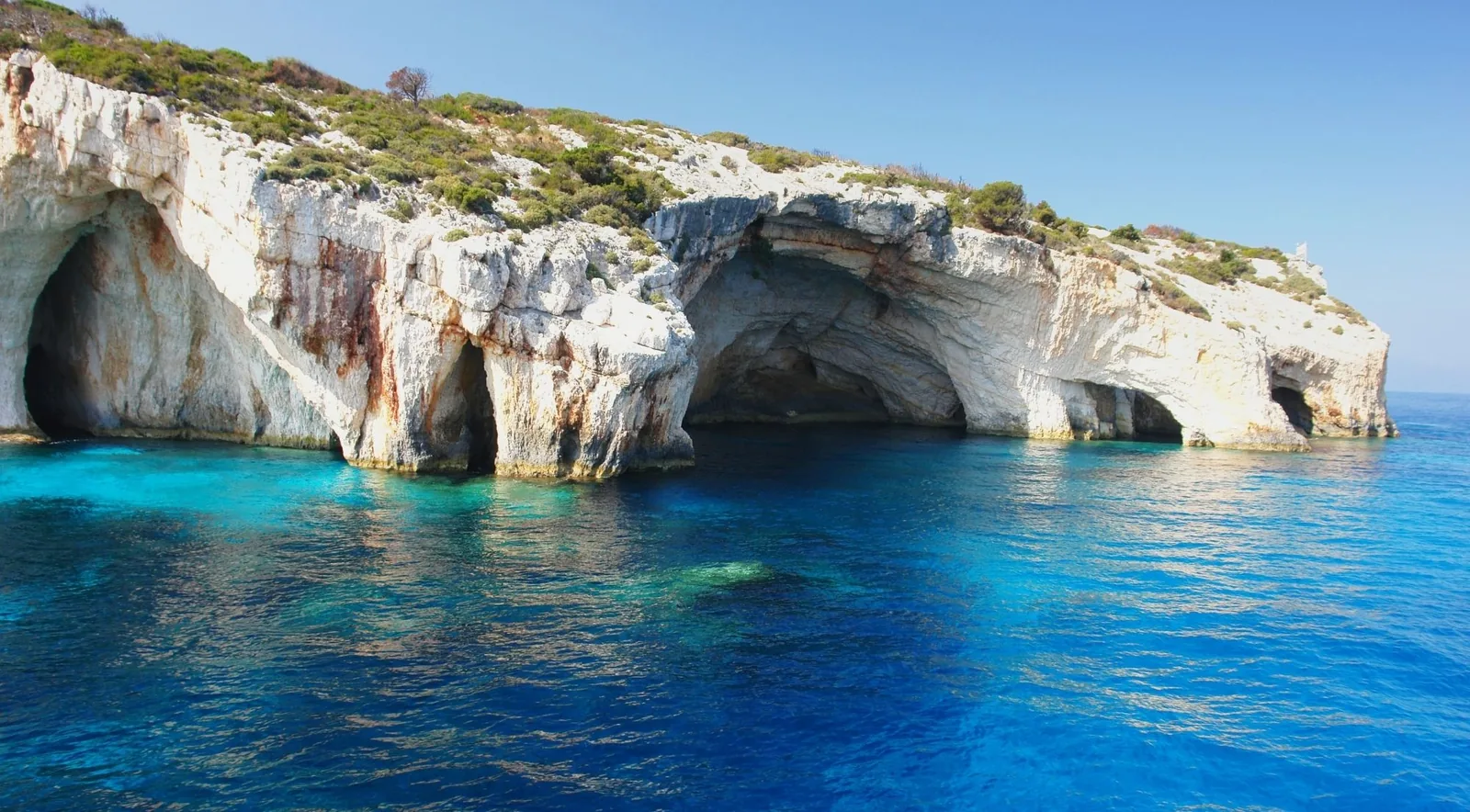 Arched cave openings in white limestone cliffs above clear turquoise water at the Blue Caves