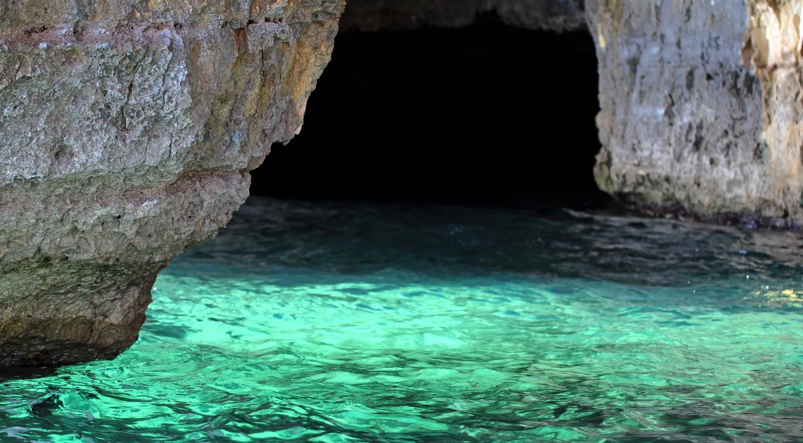 The mouth of a sea cave opening onto luminous turquoise shallows in the Blue Caves