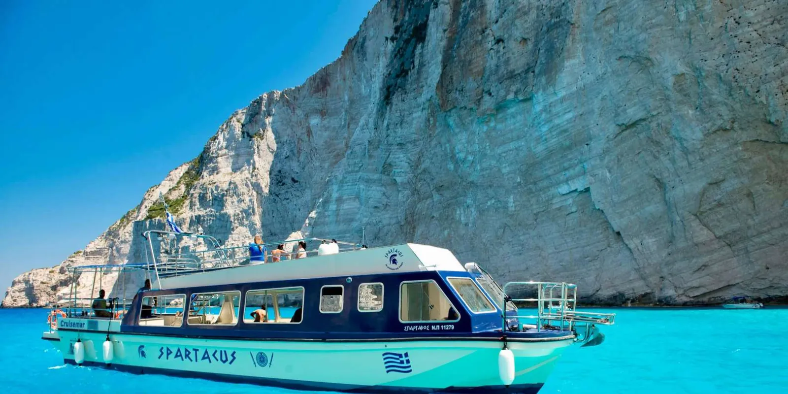 A small blue-and-white tour boat passing beneath towering pale limestone cliffs
