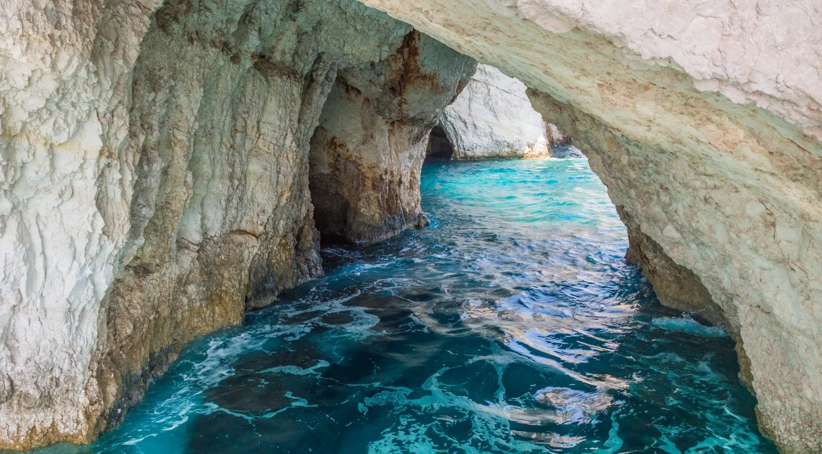 Looking out from inside a sea cave through a stone arch to bright turquoise water