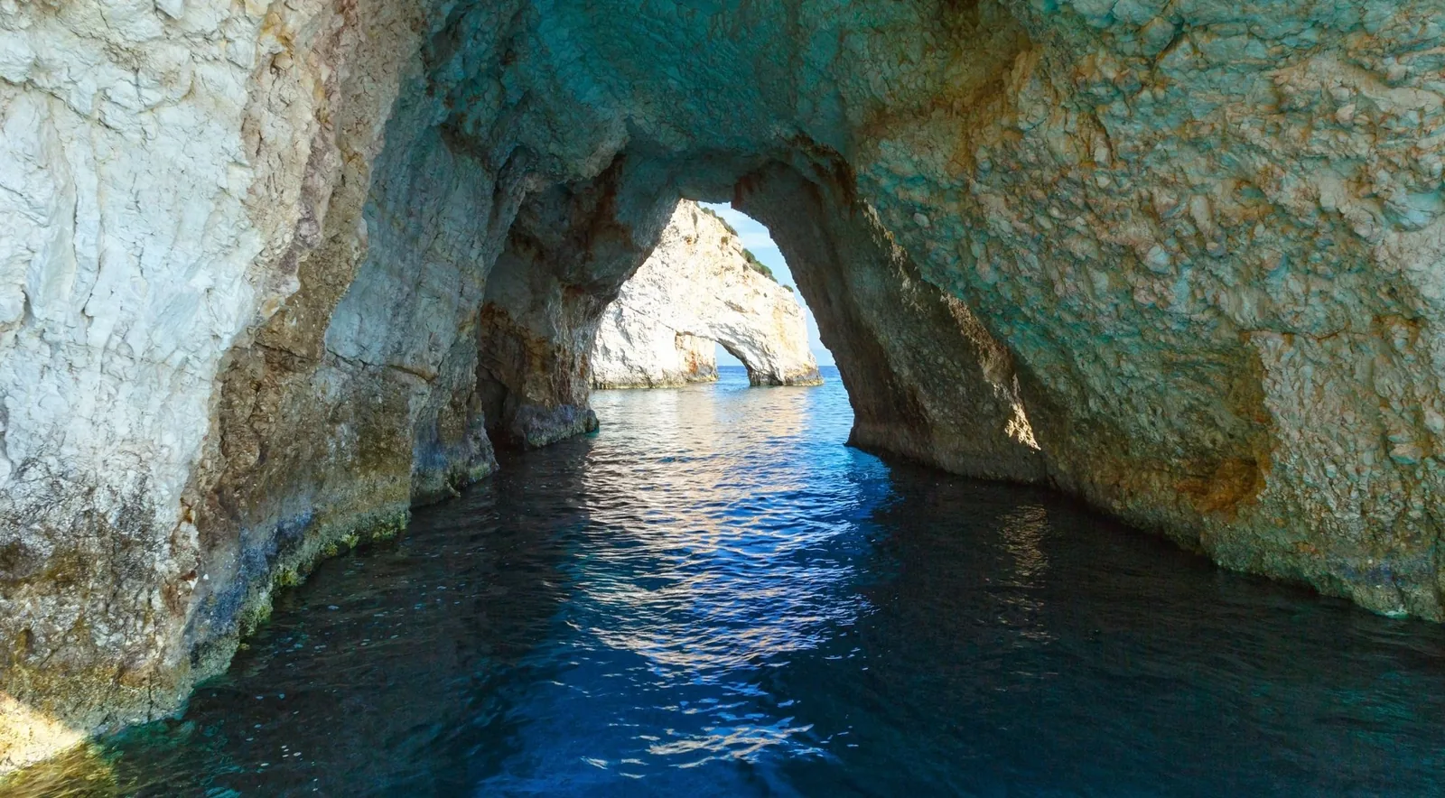 Looking out through a limestone sea arch to bright turquoise water on the north coast of Zakynthos