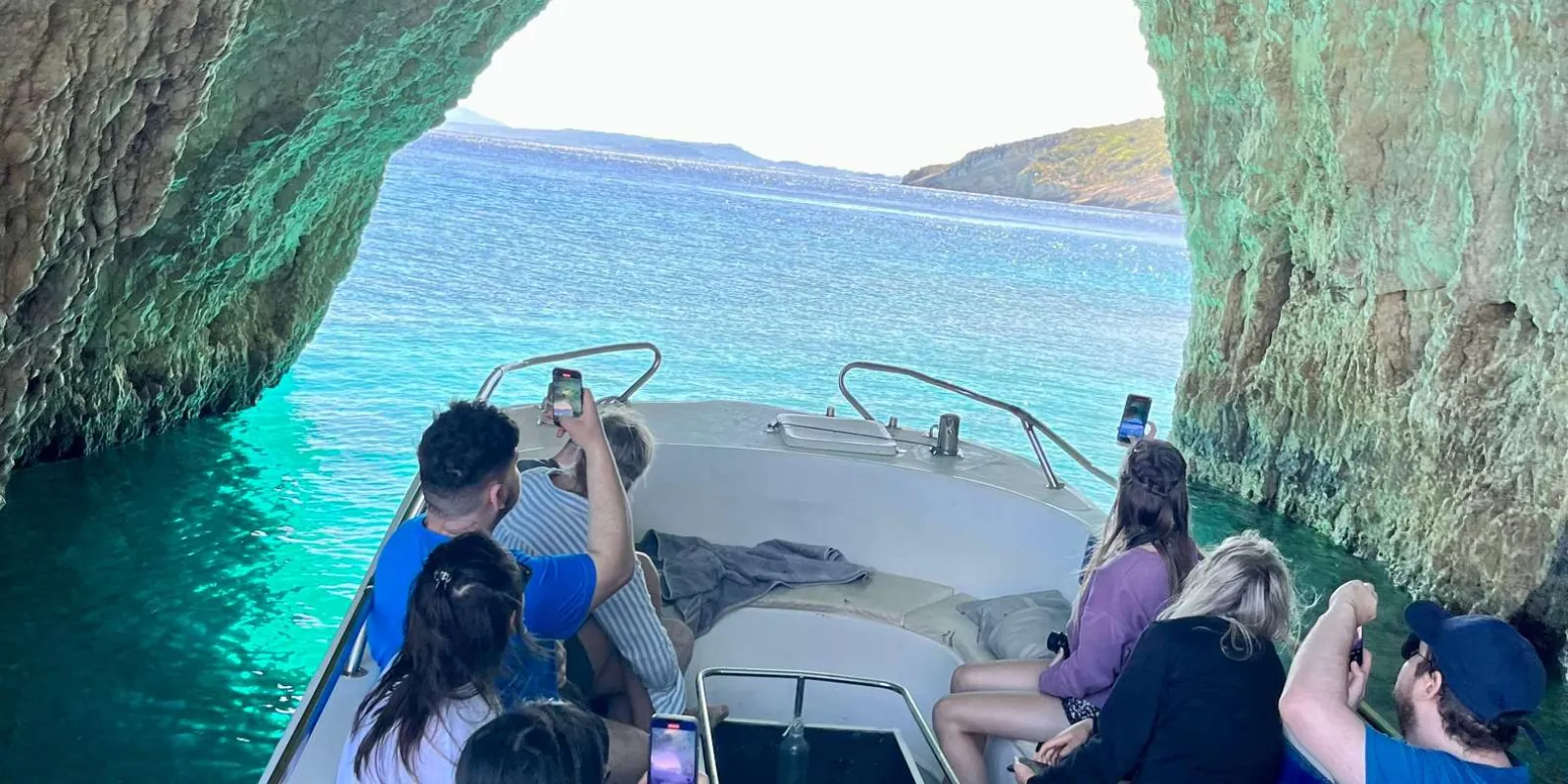 Passengers seated on an open speedboat photographing the cliffs as it passes the Blue Caves