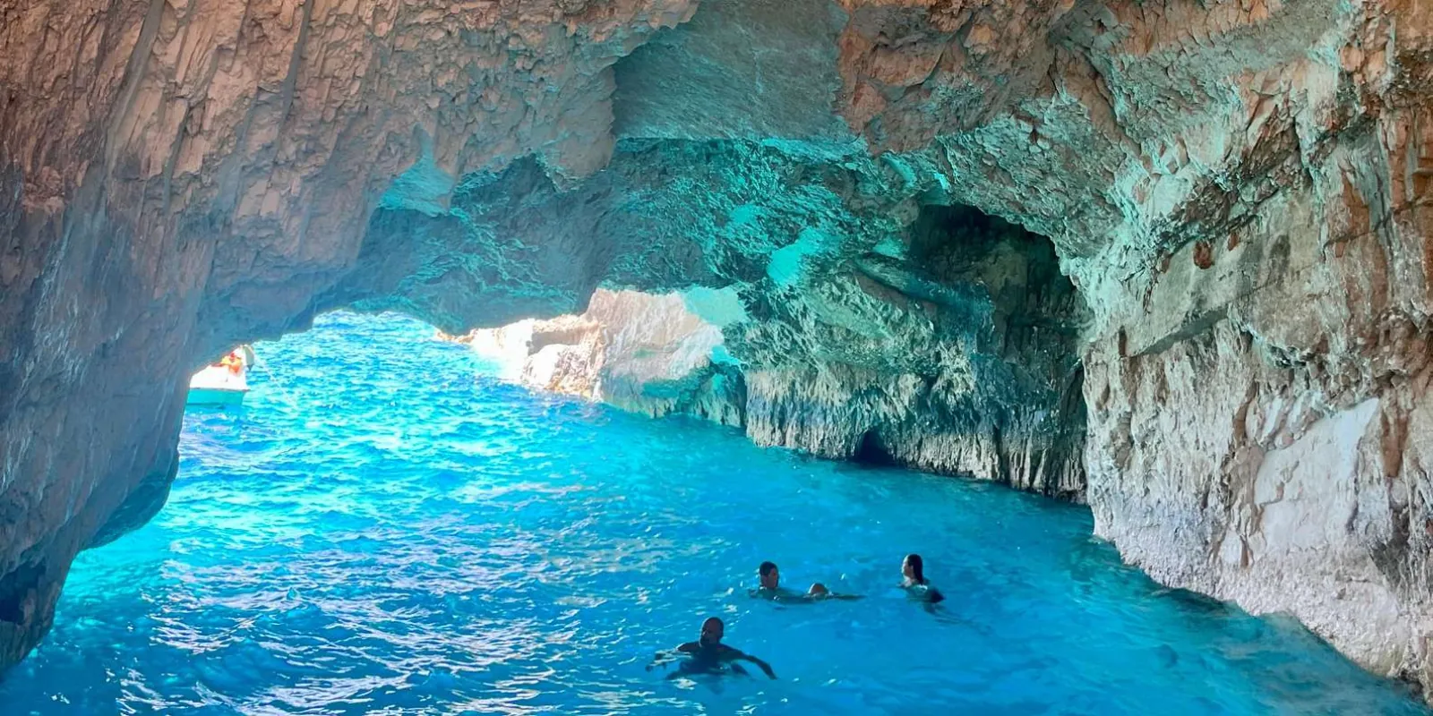 Swimmers in luminous turquoise water inside a wide sea cave
