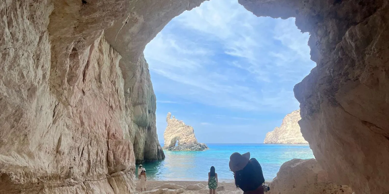 Looking out from inside a sea cave through a broad arch to sunlit water and distant rocks
