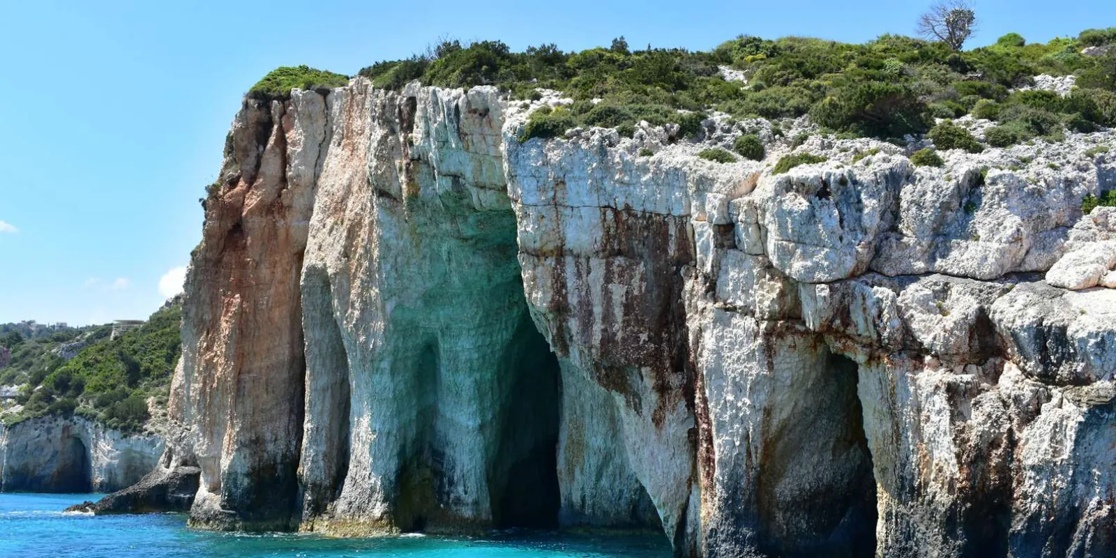 A rugged green-topped headland of pale eroded cliffs dropping into clear shallow water