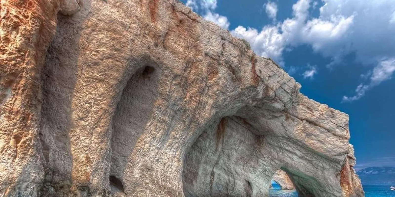 Weathered limestone arches and hollows in a sunlit cliff face above deep blue sea